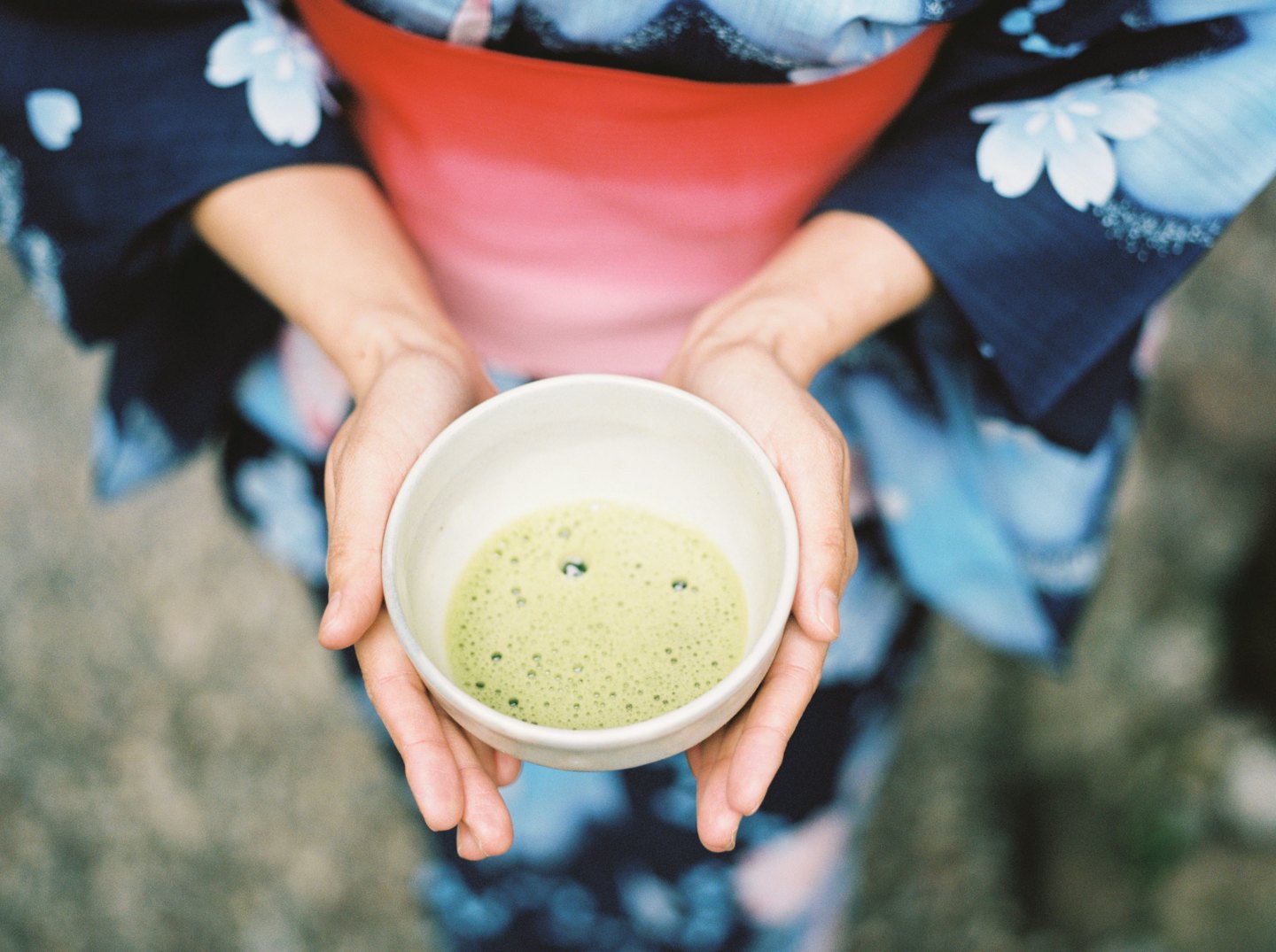 Hände halten eine Schale mit schaumigem Matcha-Tee.