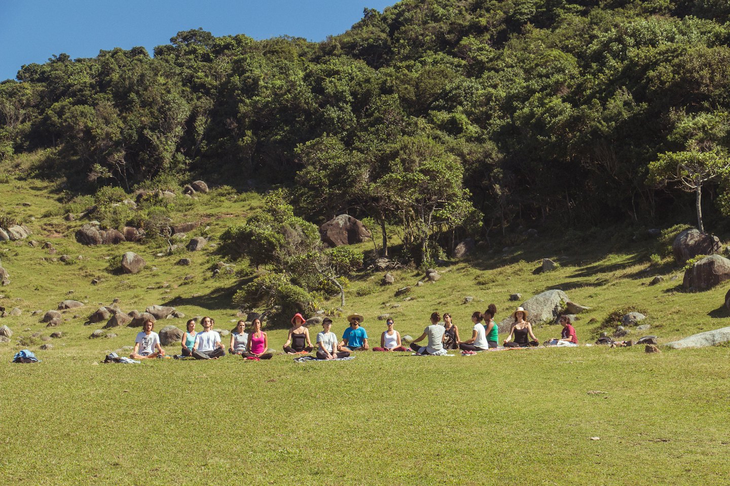 Eine Gruppe von Menschen meditiert gemeinsam auf einem grasbewachsenen Hügel.